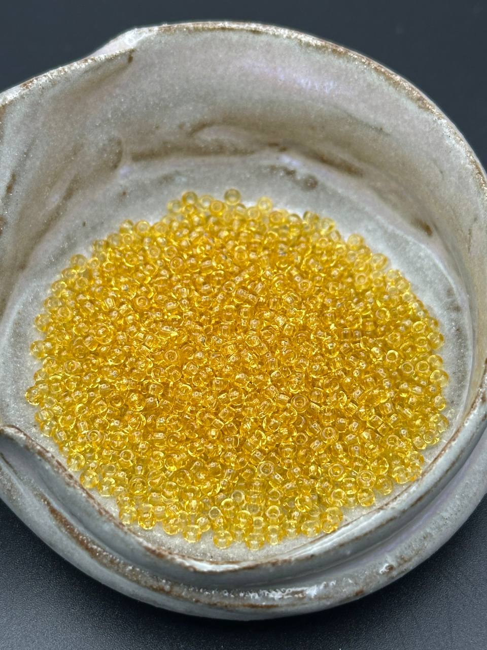 Close-up of yellow beads in a ceramic container on a dark background