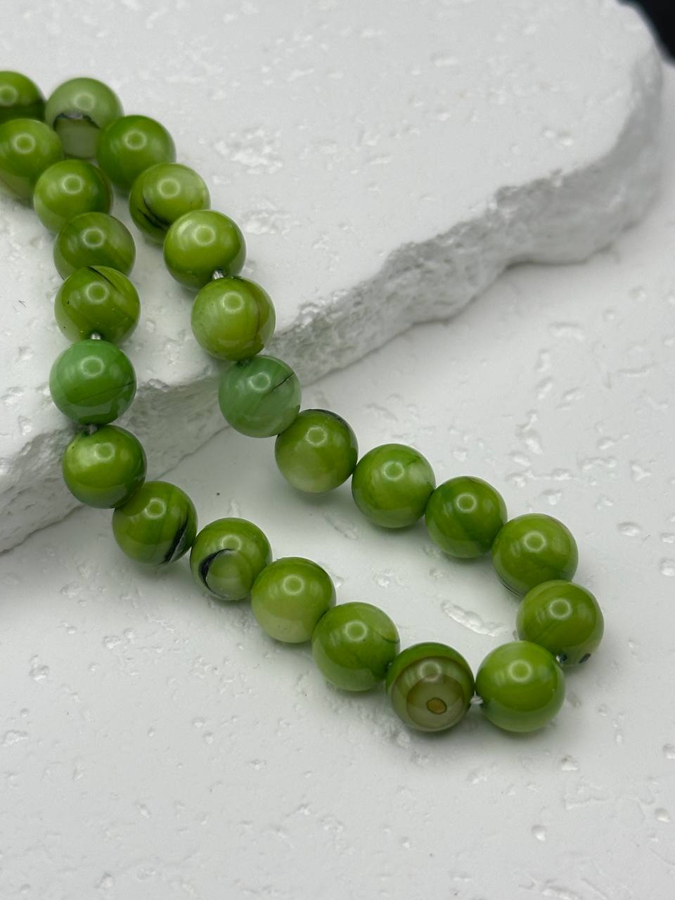 Green beaded necklace on a textured white surface