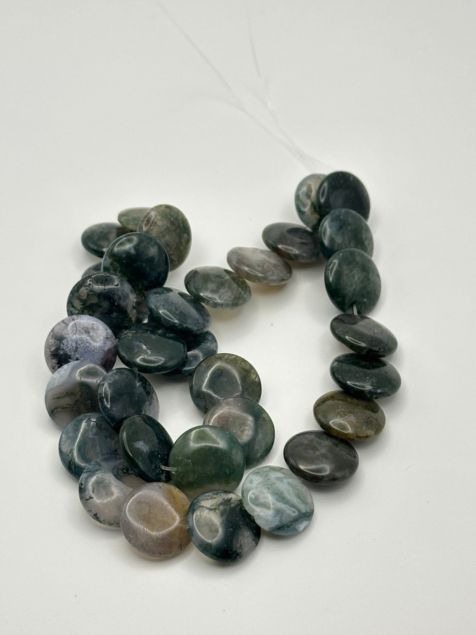 a string of disc shaped moss agate beads on a white surface