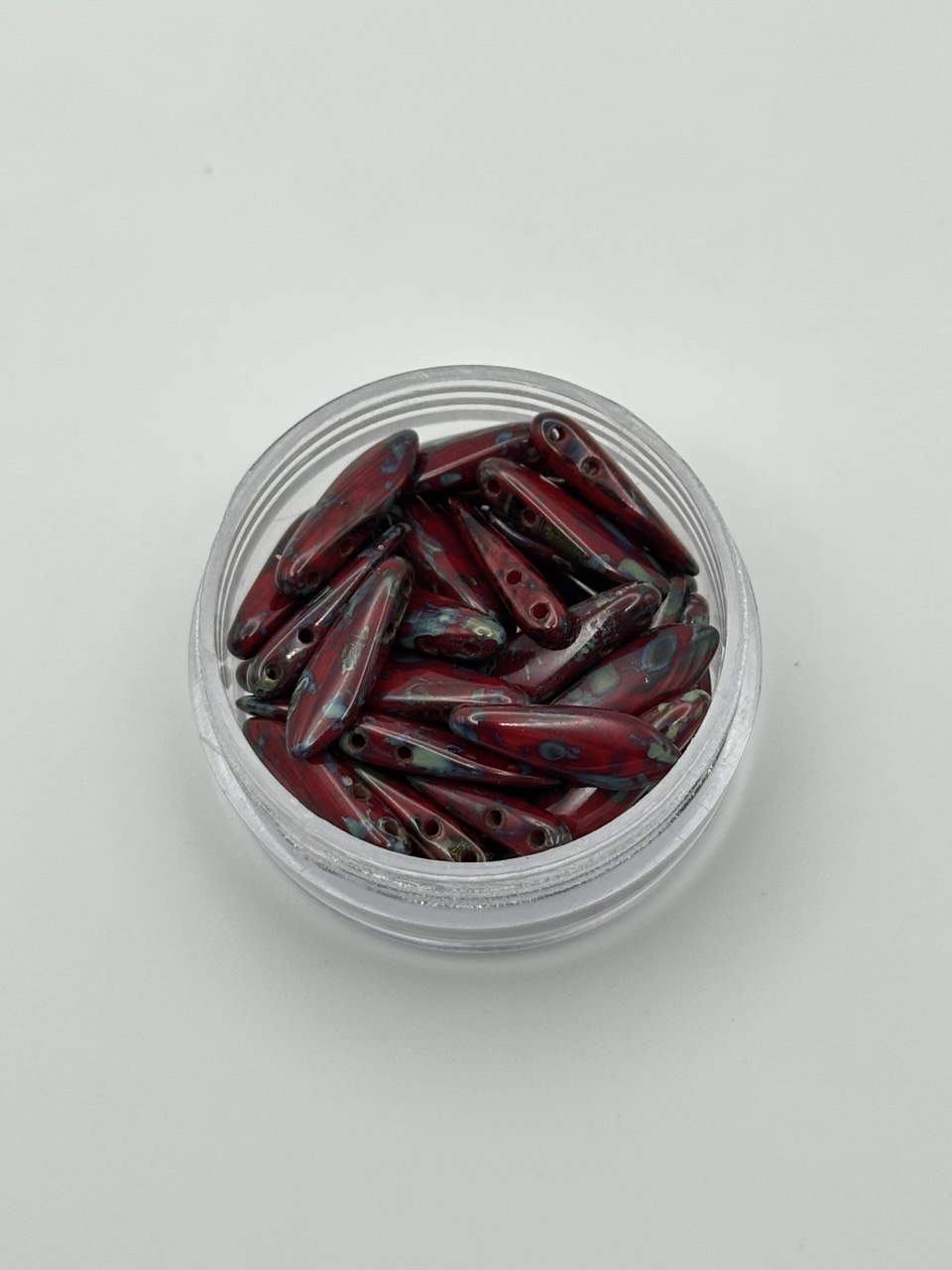 Clear container with red and black dagger beads on a light gray background