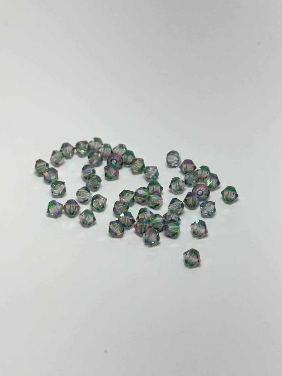 A small cluster of faceted iridescent beads scattered on a plain light gray background.