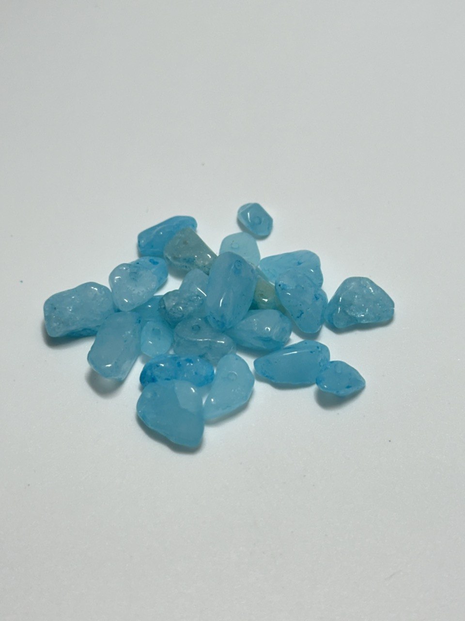 A small pile of tumbled blue quartz chips or pebbles on a plain light gray background.