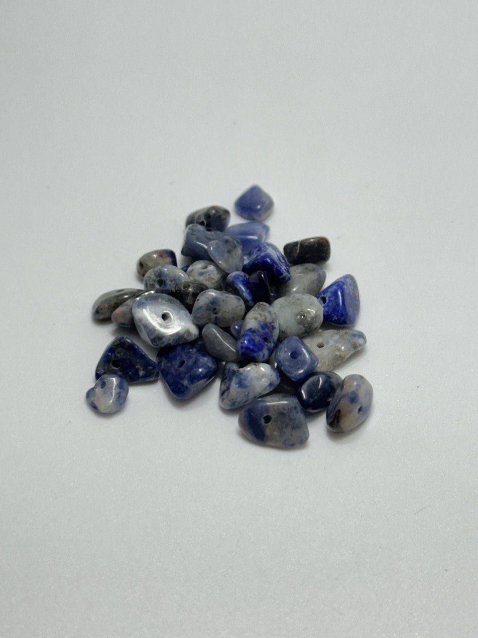 A small pile of polished blue and white tumbled gemstone beads with small holes, arranged on a plain light gray background.