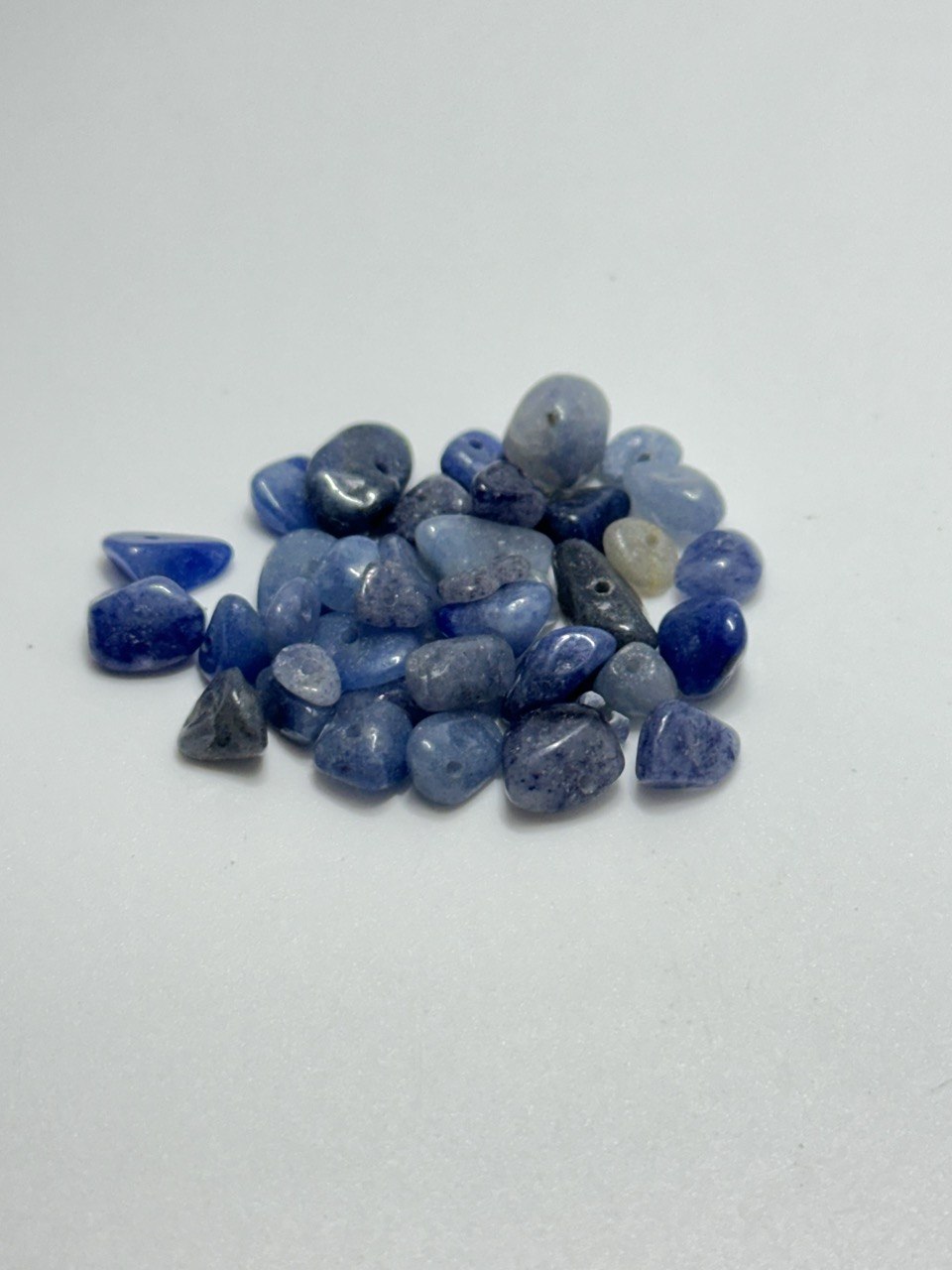 A small pile of polished blue tumbled blue aventurine on a plain light gray background.