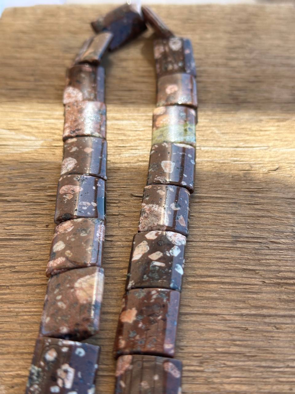 Brown and green rhyolite rectangle beads on wooden surface