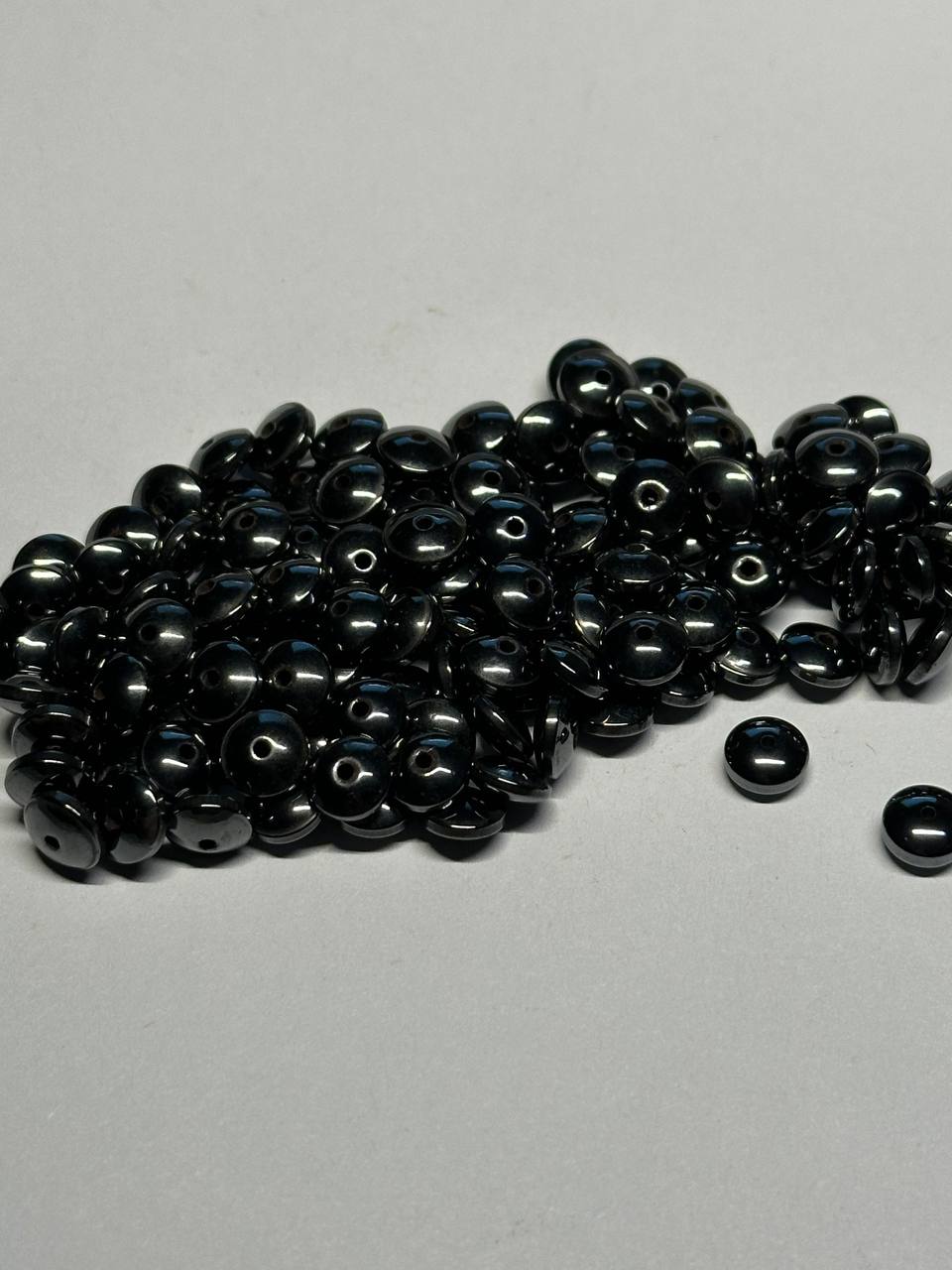 Black hemalyke rondelle beads scattered on a gray surface