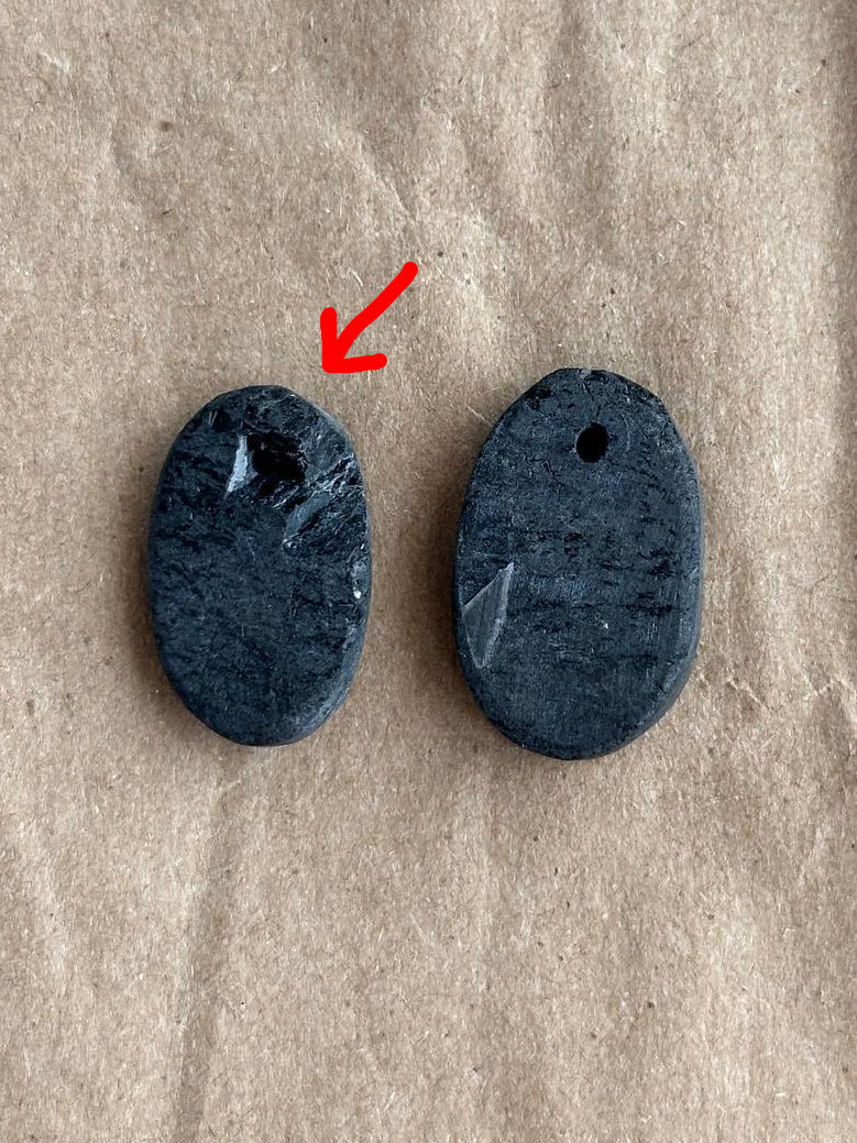 Two dark gray oval stone pendants with holes, placed on a textured brown kraft paper background.