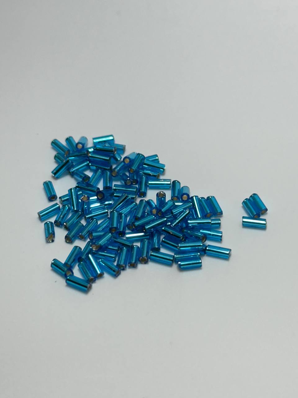 A small pile of blue silver lined bugle beads on white background