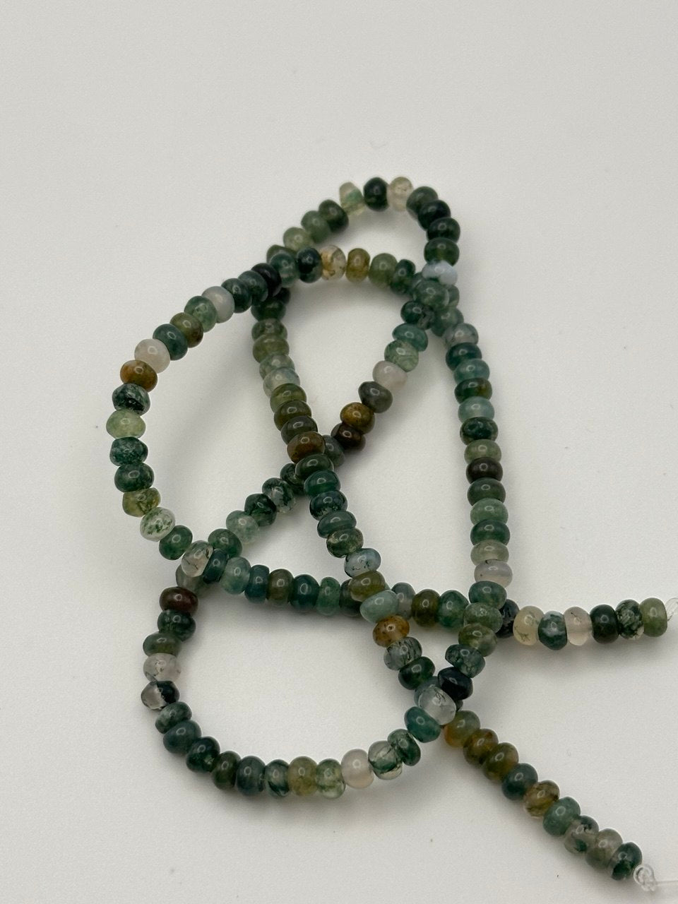 green and white rondelle beads on a white surface