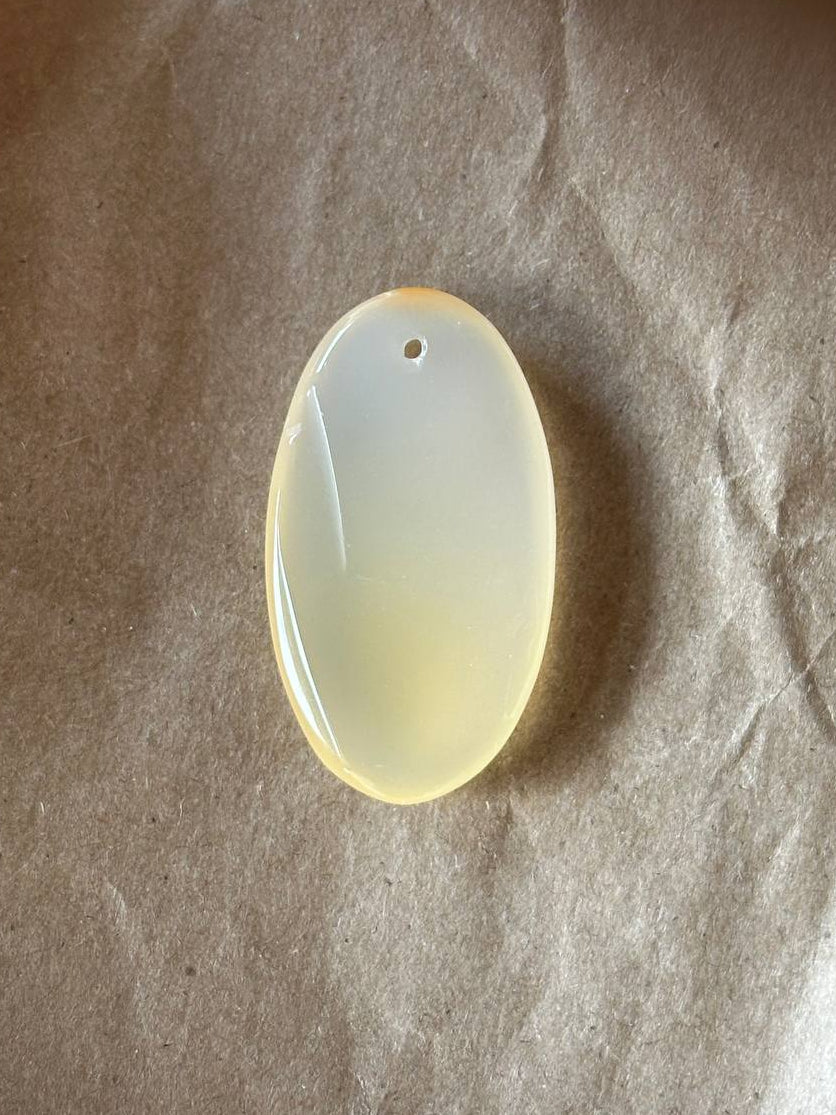 An oval translucent pendant with a small hole at the top, resting on a textured brown paper background.