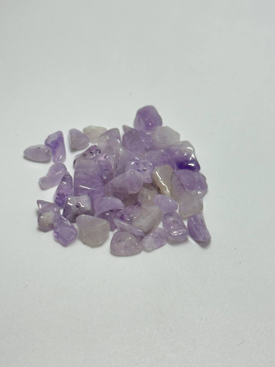 A small pile of rough, tumbled purple amethyst stones on a plain light gray background.