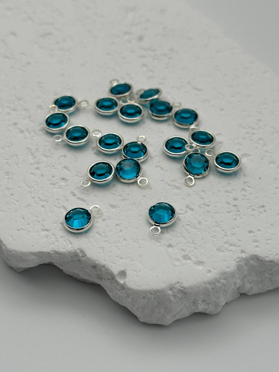 Silver jewelry components with blue crystals on a textured stone surface