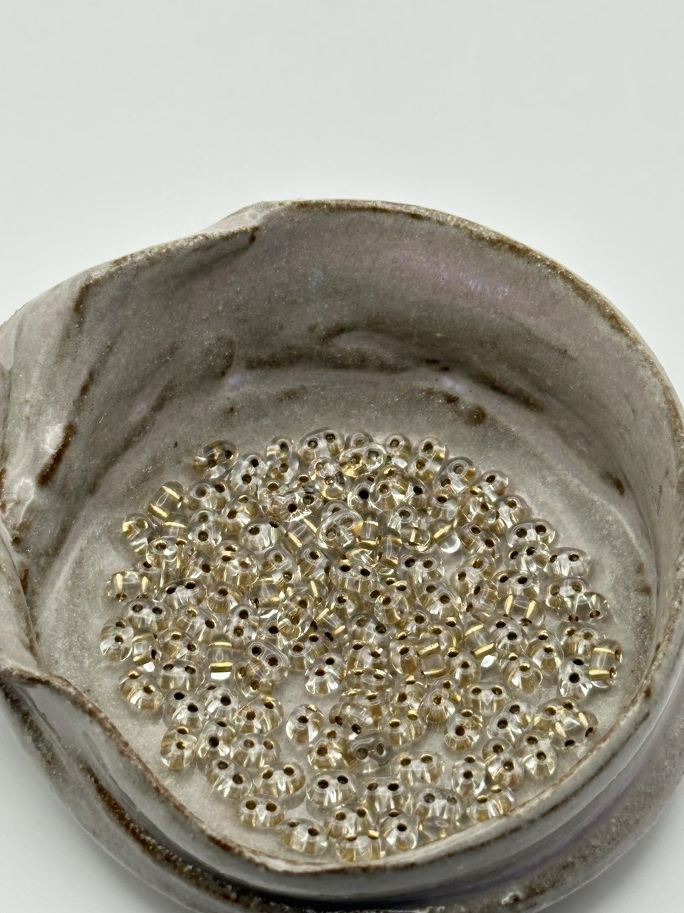 Small container filled with small twin 2-hole beads on a light gray background