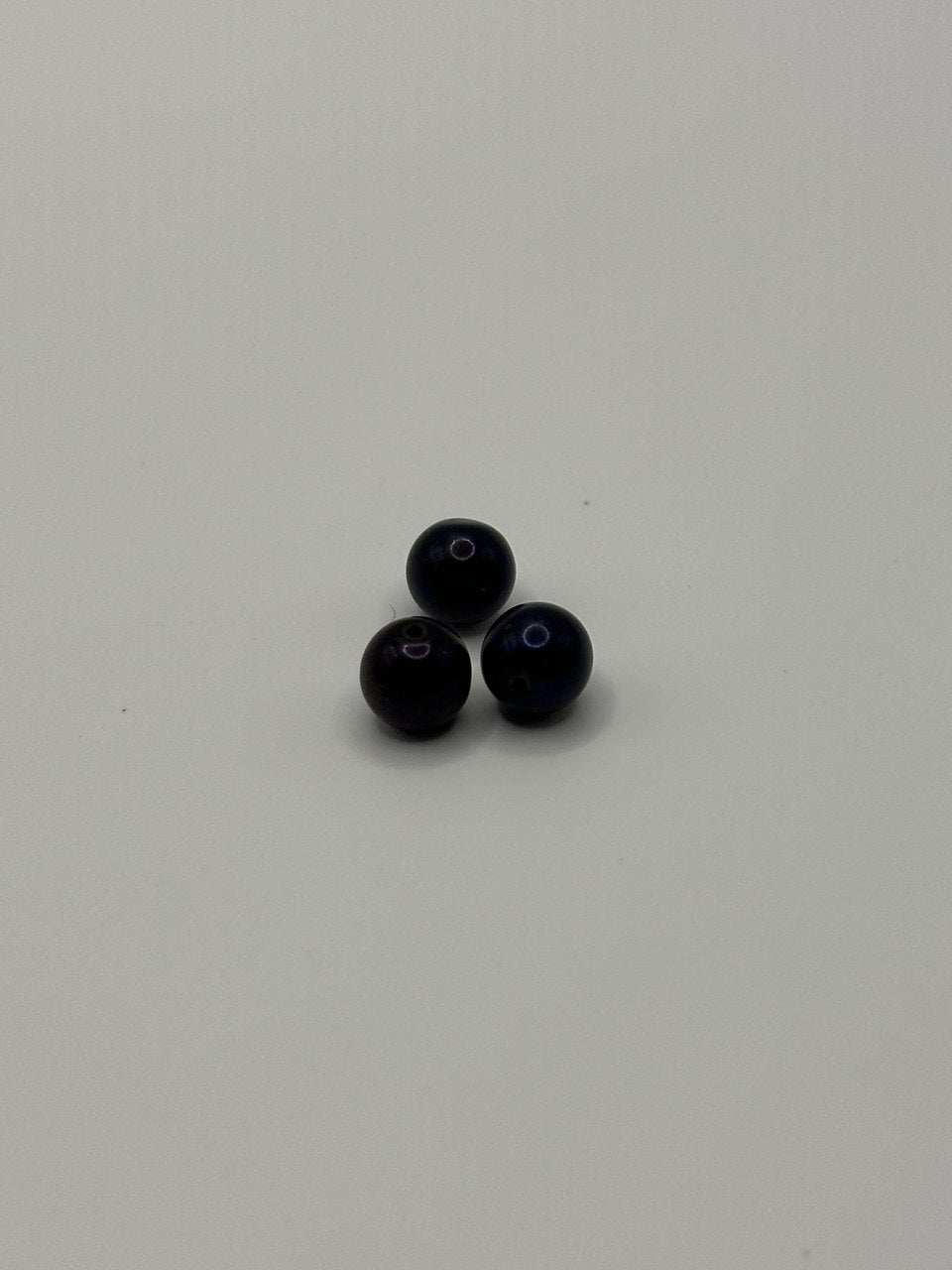 Three dark purple beads on a light gray background