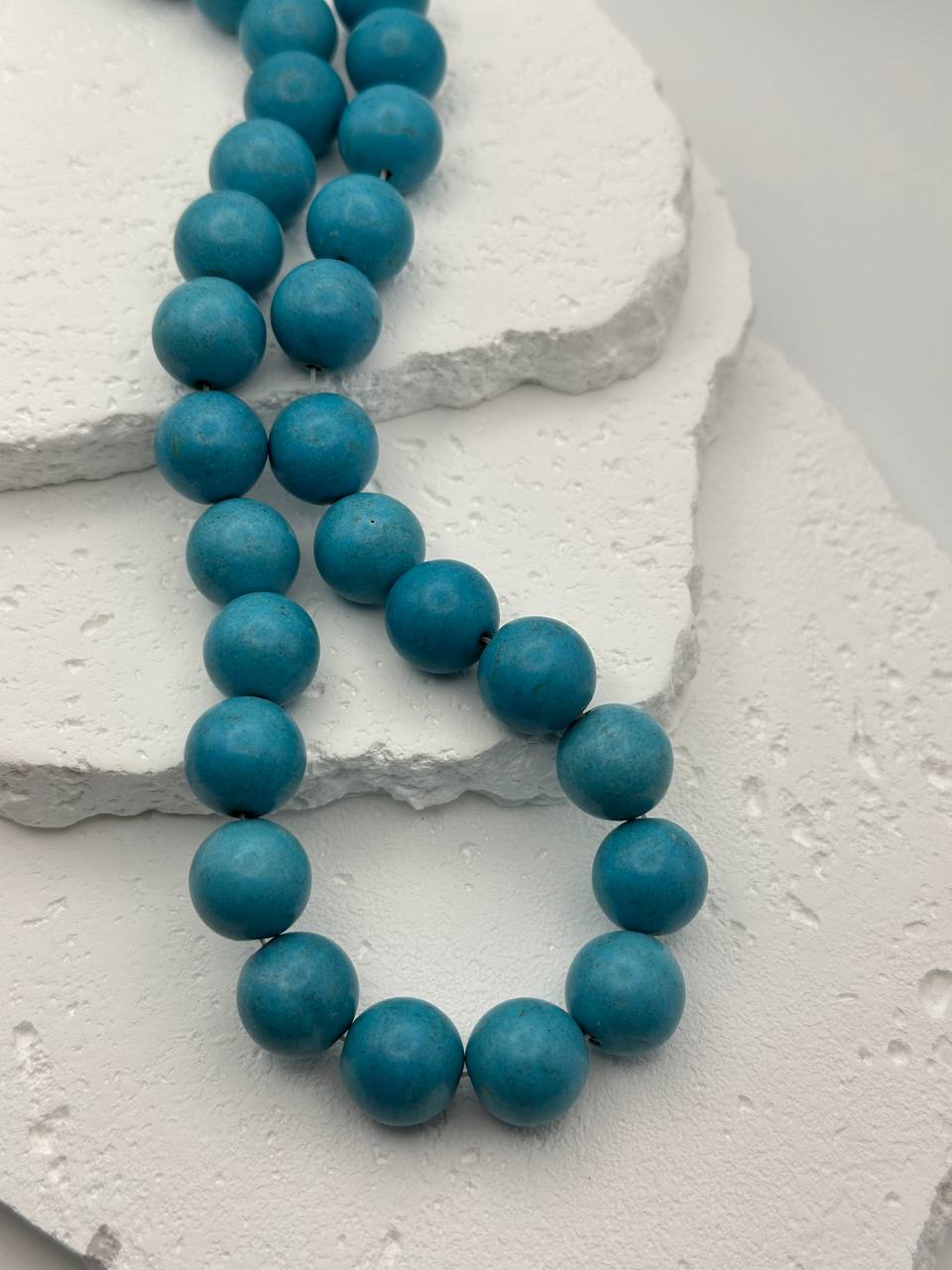 Turquoise colored beads on a textured white surface