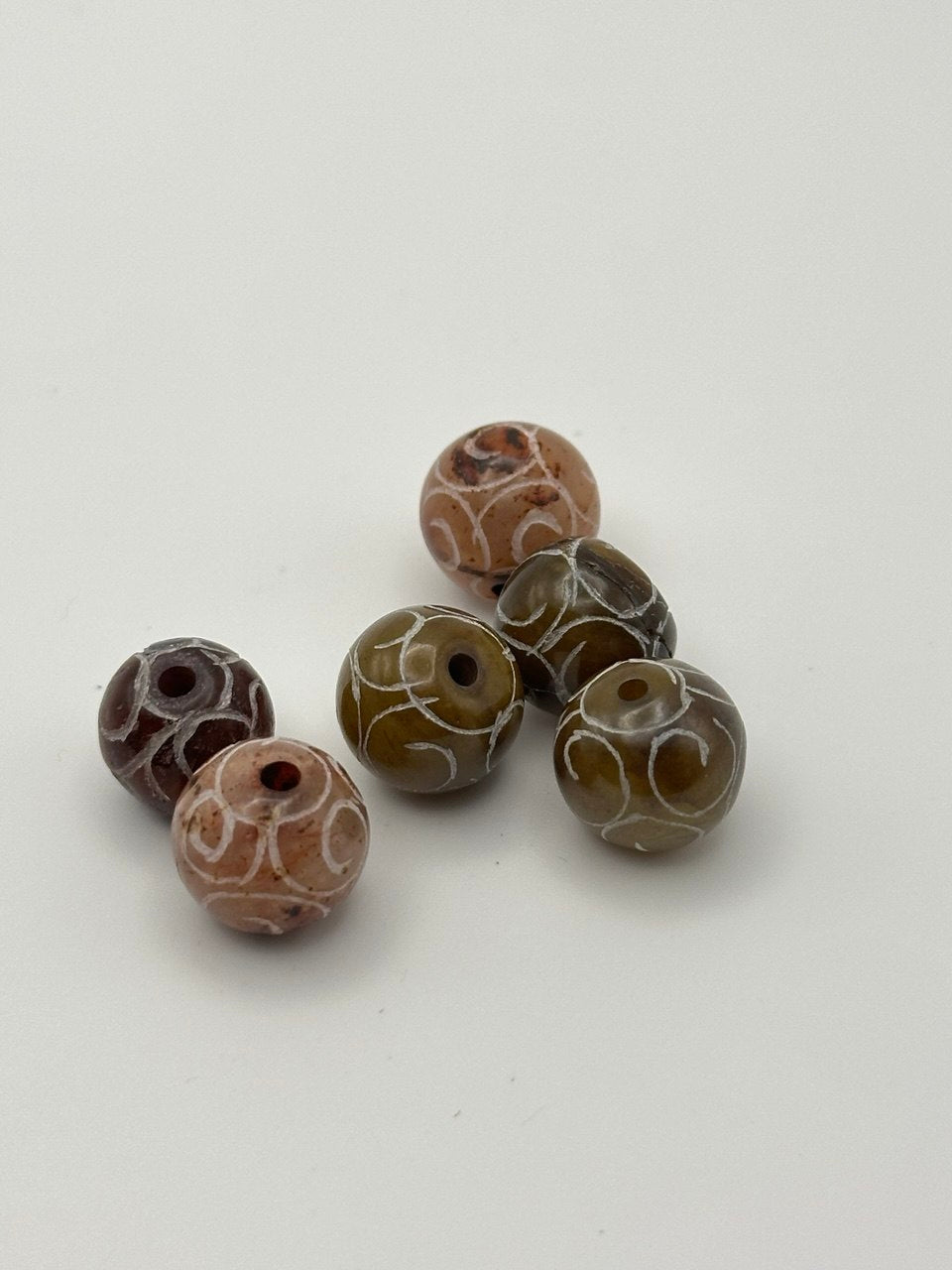 Set of six brown and white patterned beads on a light gray background