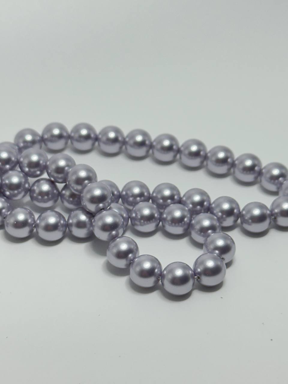 A strand of glossy, lavender-purple faux pearl beads arranged in loops on a plain light gray background.