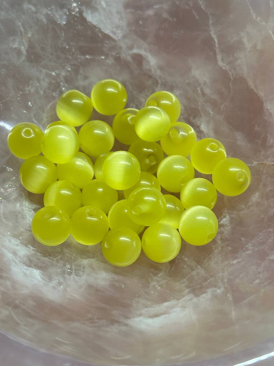 Yellow cat eye beads in a clear bowl on a marble surface