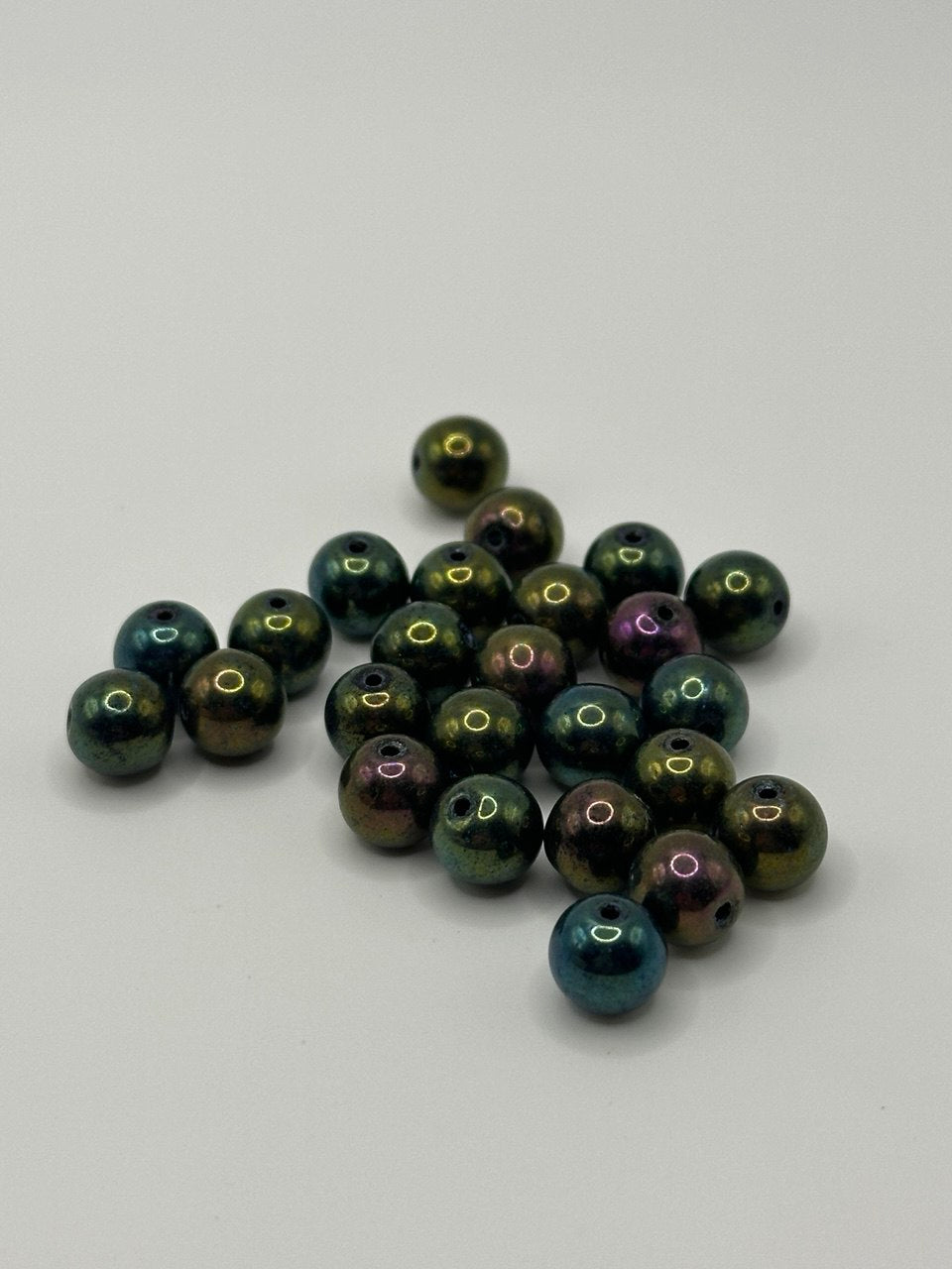 Collection of dark green metallic beads on a light gray background