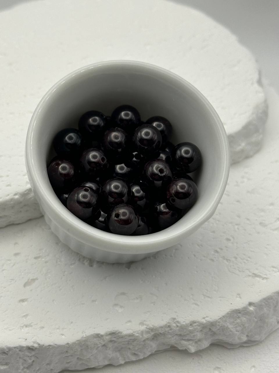 White bowl filled with dark red beads on a textured white surface