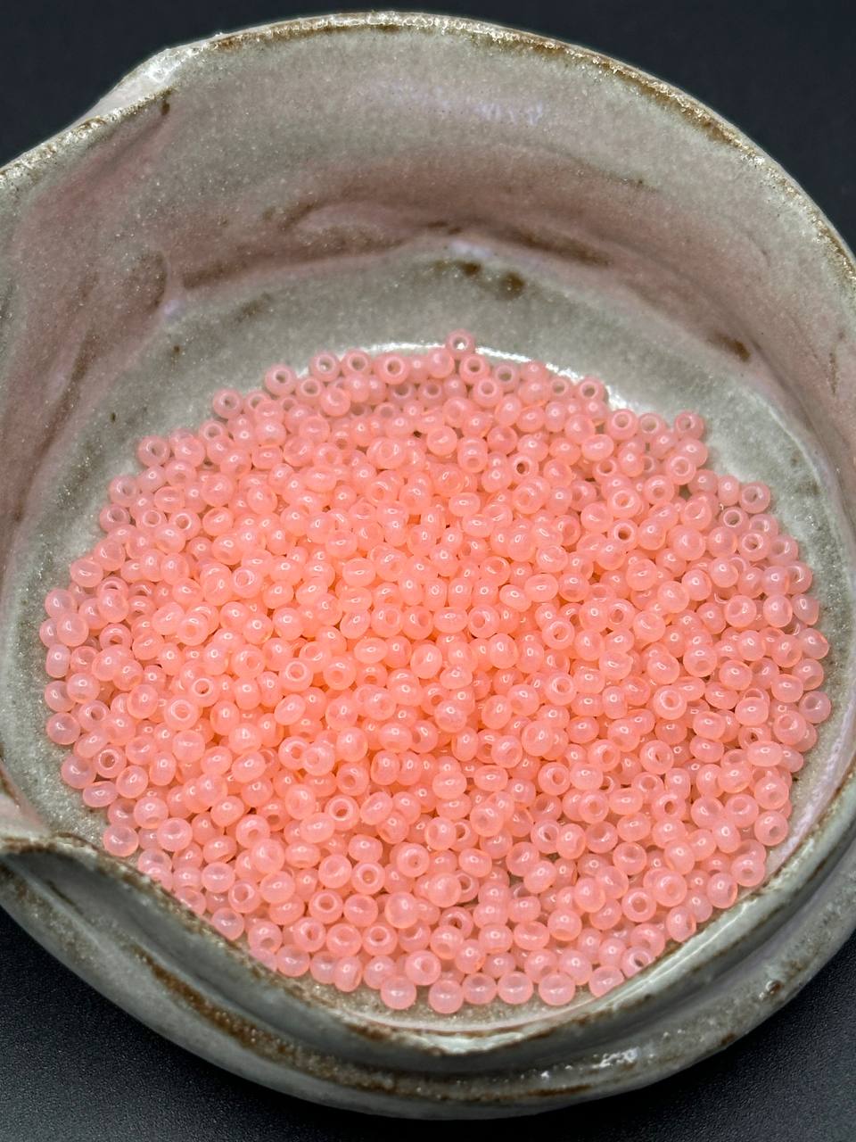 Small pink beads in a ceramic container on a dark background