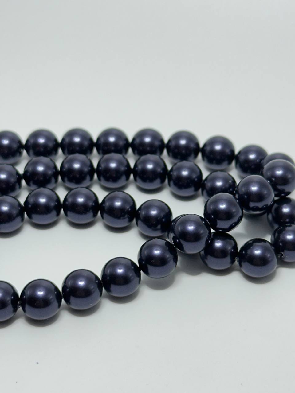 A strand of glossy, dark navy blue round beads arranged in loops on a plain light gray background.