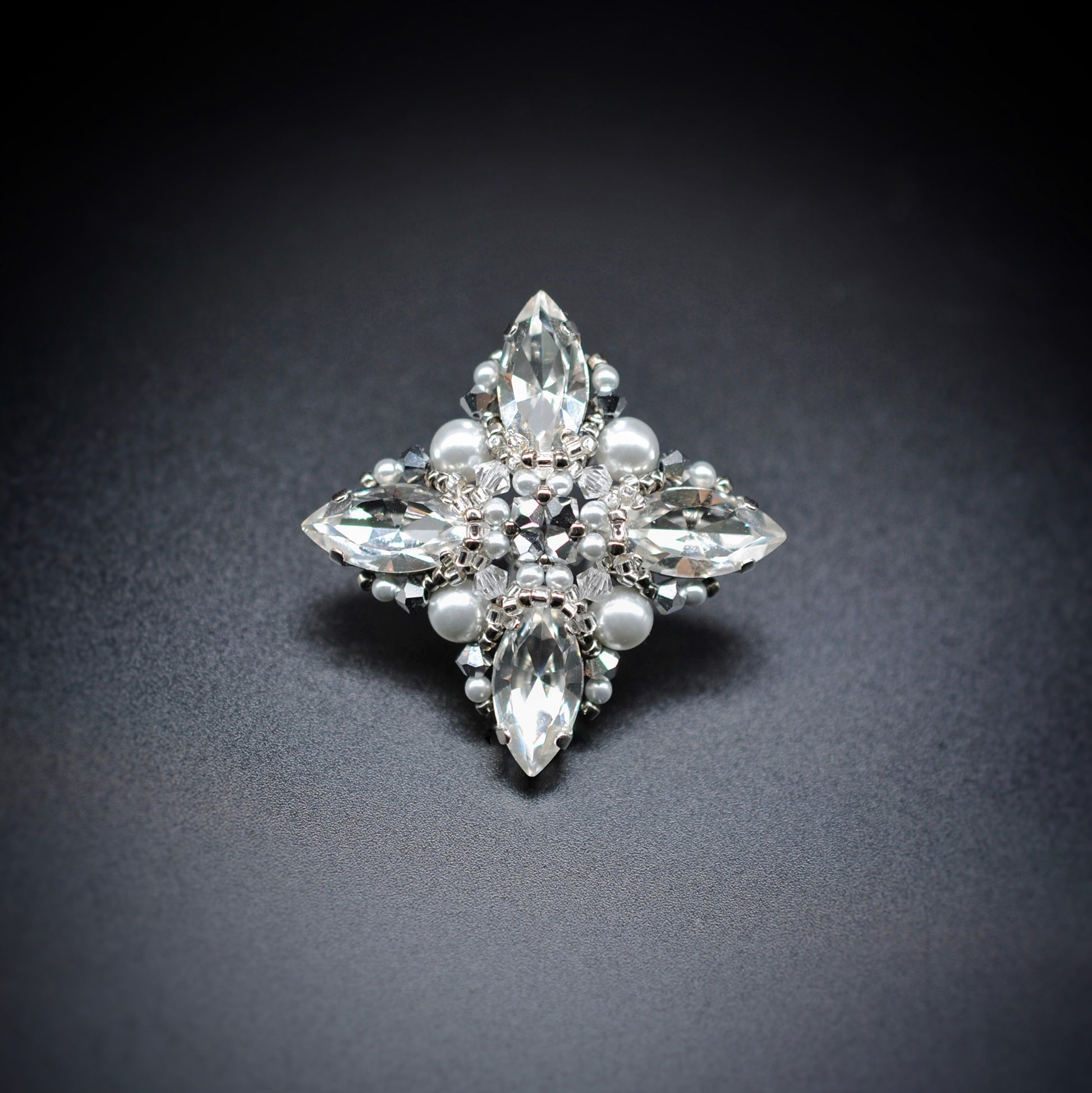 A vintage-style silver starburst brooch featuring clear marquise-cut crystals, round pearl-like beads, and small silver beads, displayed on a dark gray background.