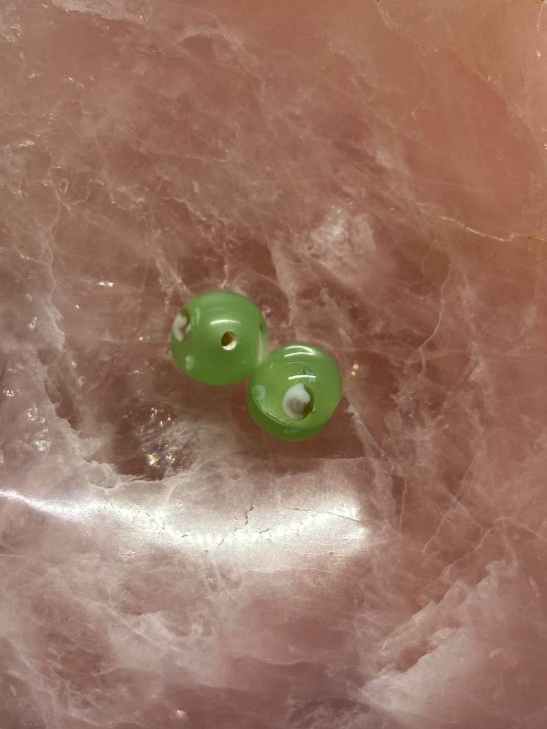 Two green beads on a textured pink surface