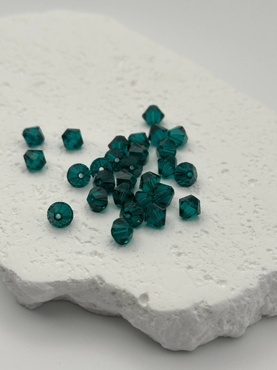Emerald bicone beads on a textured white surface