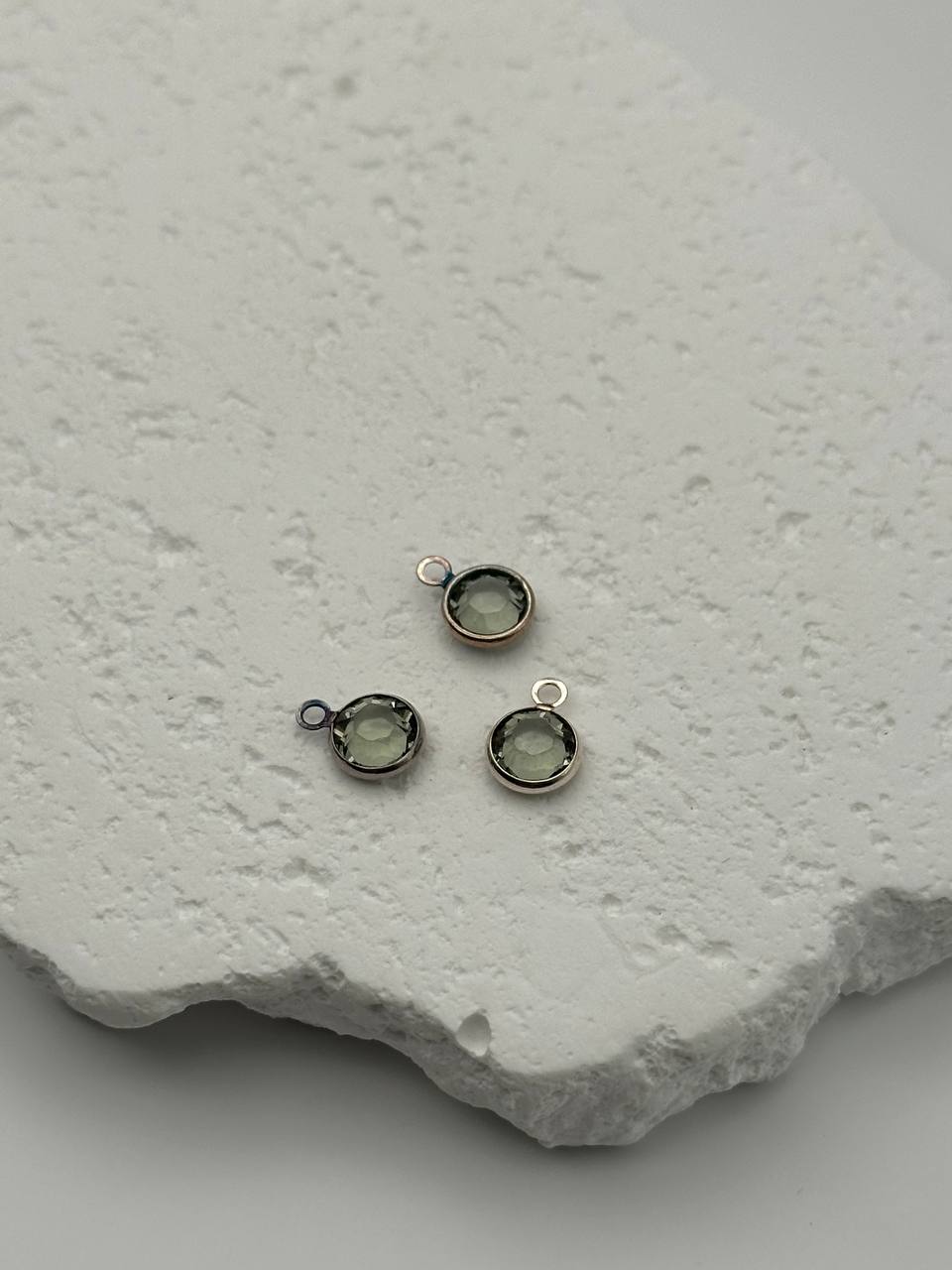 Three small silver jewelry components with chatons on a textured white surface