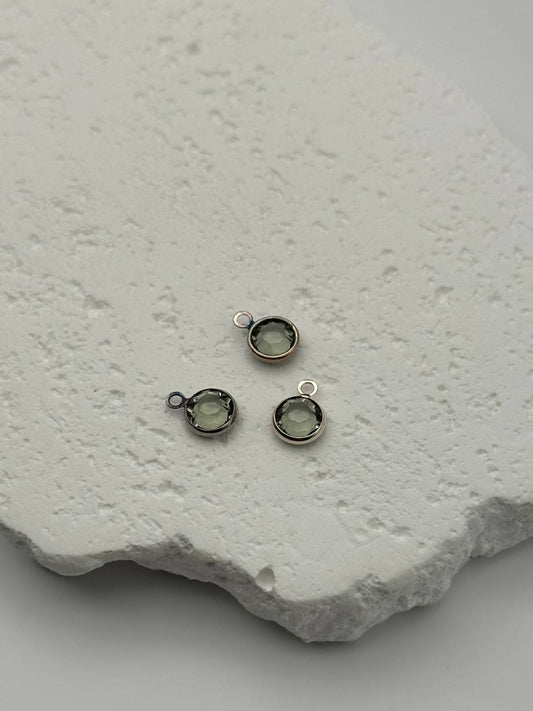 Three small silver jewelry components with chatons on a textured white surface