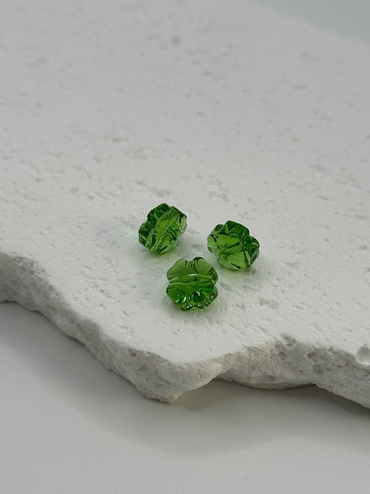 Three green clever shaped beads on a textured white surface