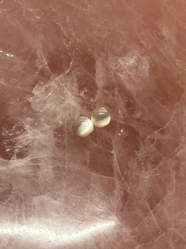 Two small cat's eye beads on a pinkish marble surface