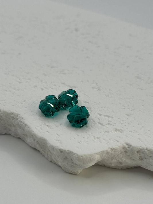 Three emerald clover shaped beads on a textured white surface
