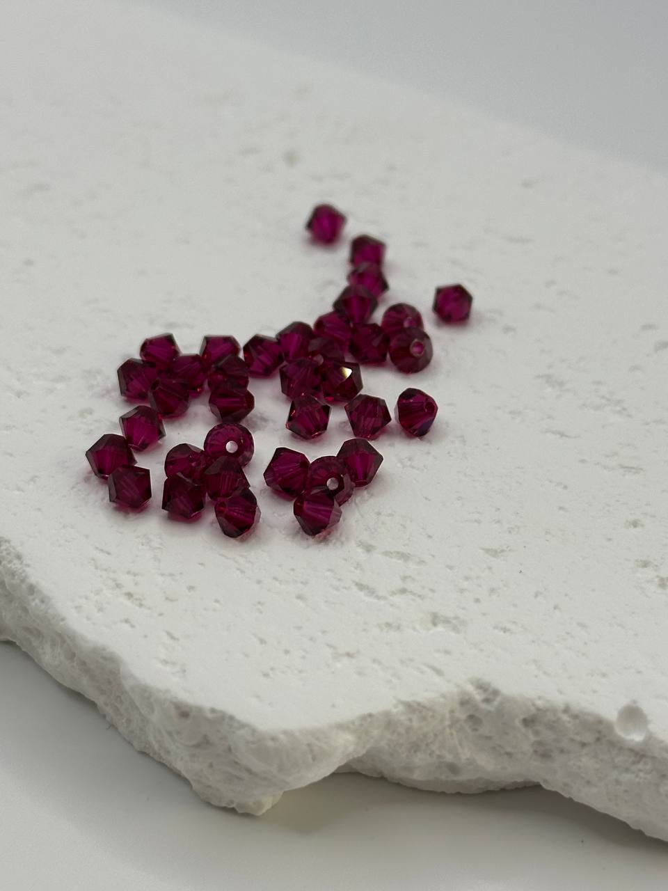 Ruby bicone beads on a textured white surface