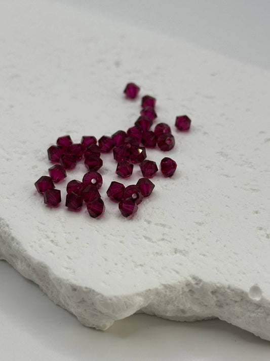 Ruby bicone beads on a textured white surface