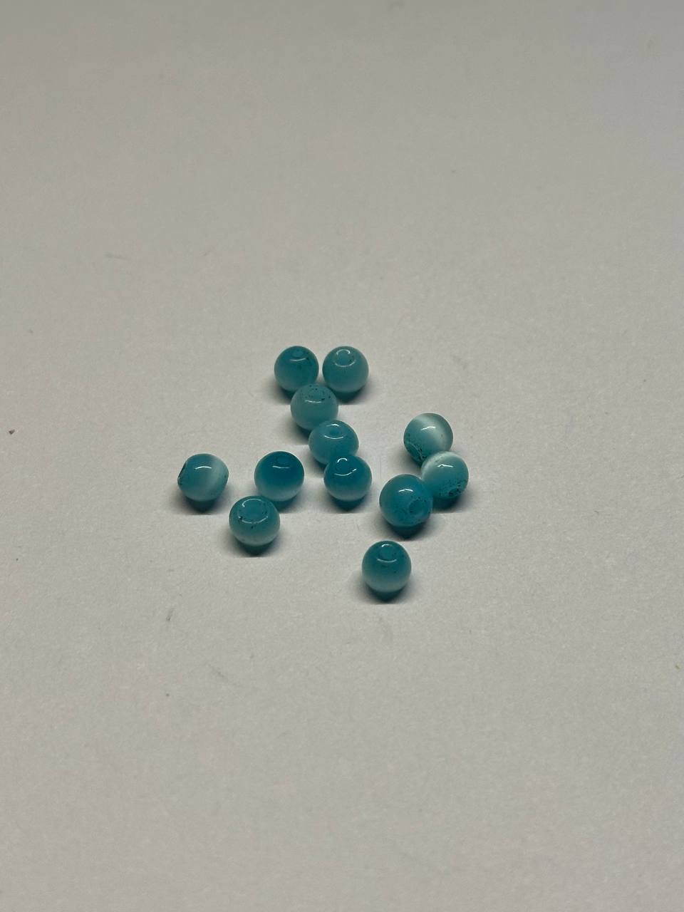Teal beads scattered on a white surface