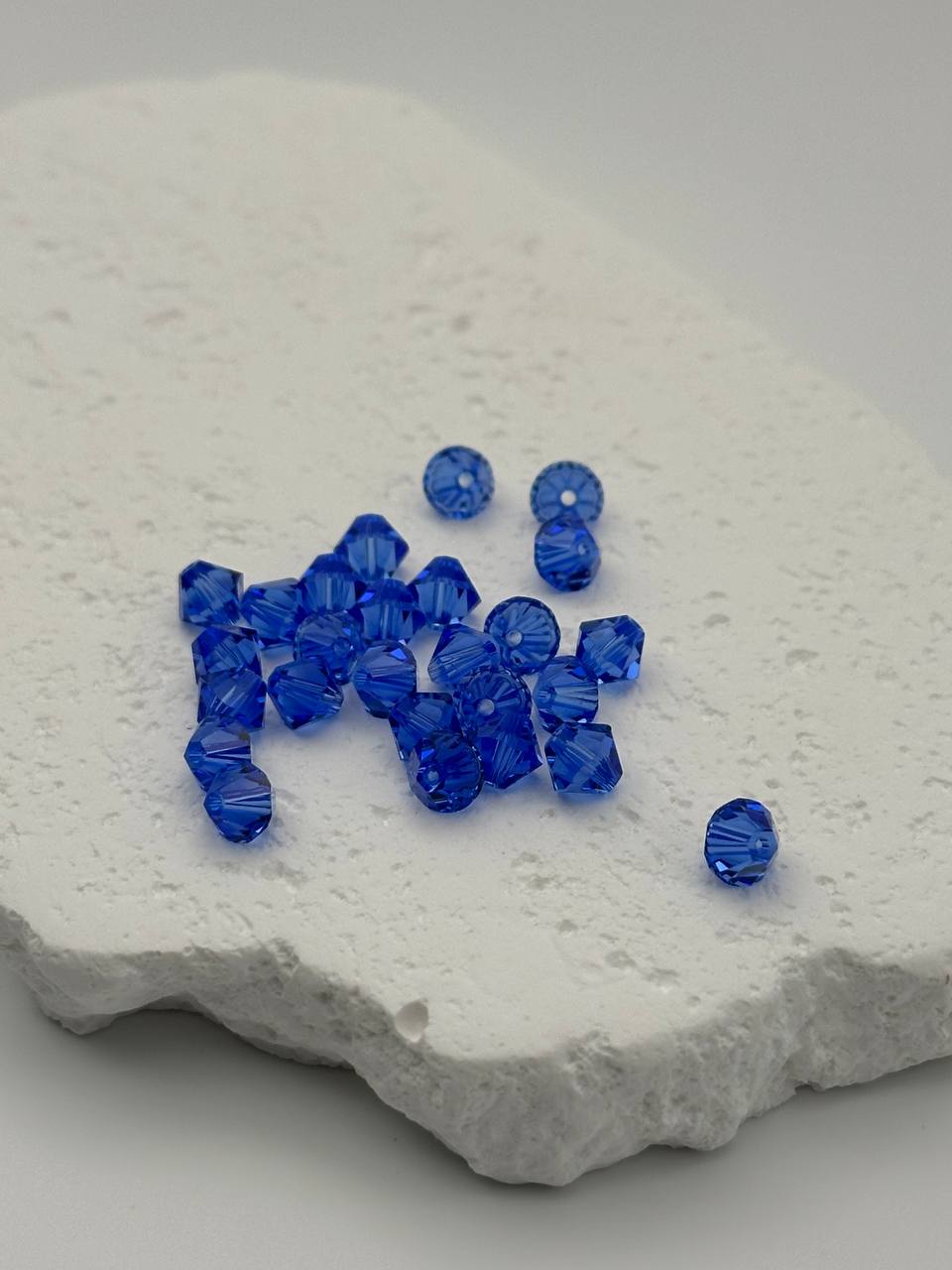 A small pile of sapphire bicone beads on white surface