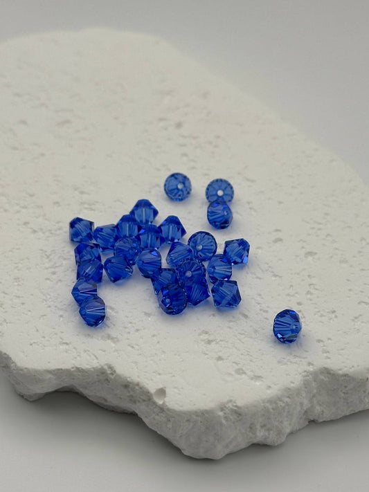 A small pile of sapphire bicone beads on white surface