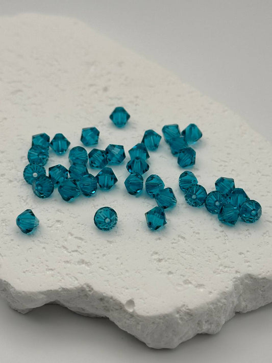 Blue zircon bicone beads on a textured white surface