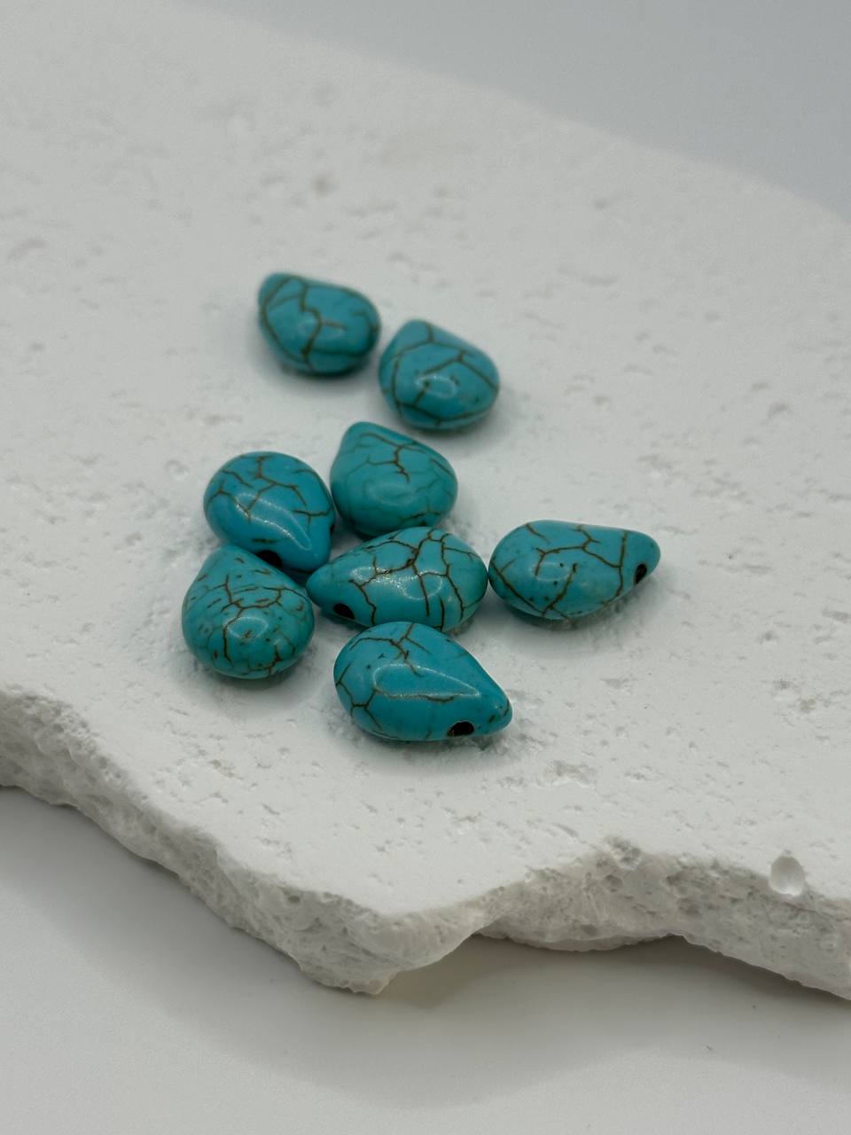 Turquoise teardrop beads on white surface