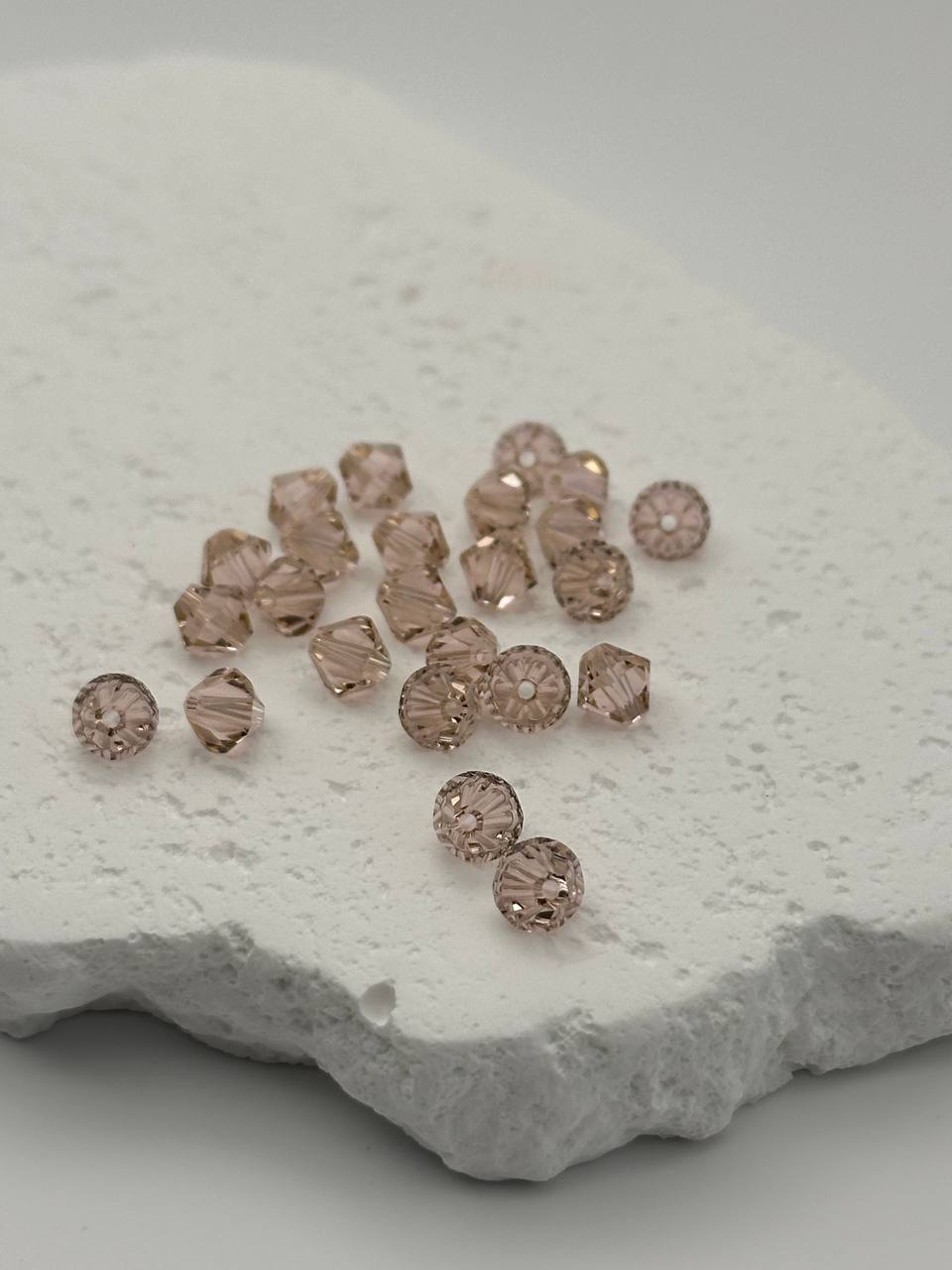 Vintage rose bicone beads on a textured white stone surface