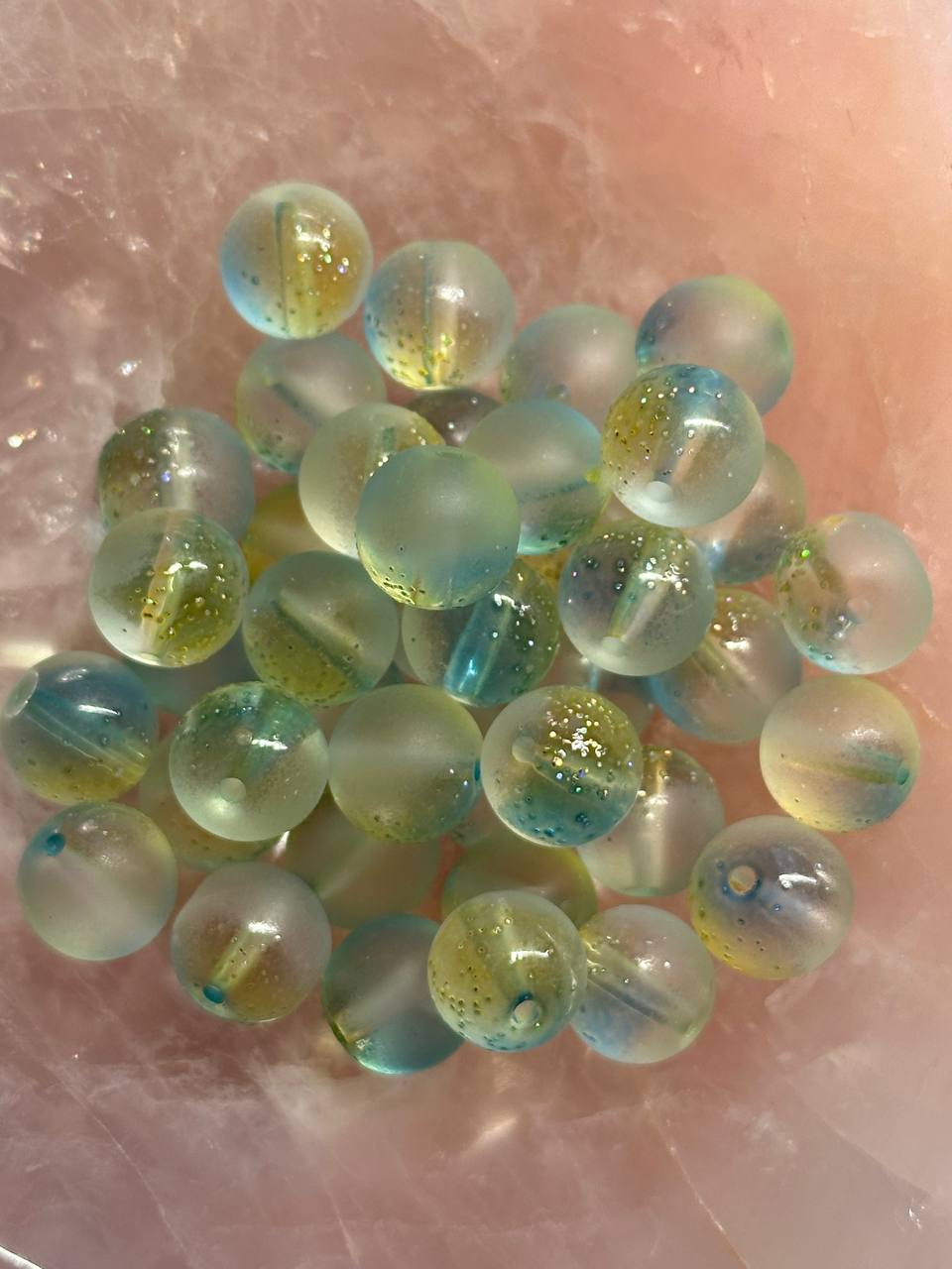 Matte blue green and yellow beads with gold flecks on a pink surface
