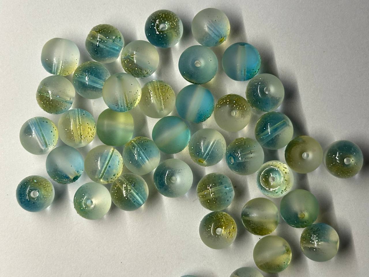 Collection of green and blue glass beads on a light gray background