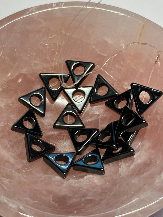 Black triangular beads with central holes on a reflective surface