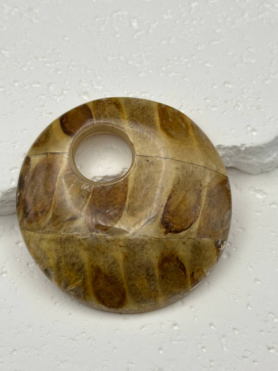 Round stone object with a central hole on a textured white background