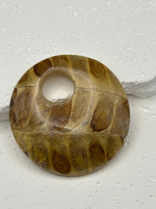 Round stone object with a central hole on a textured white background
