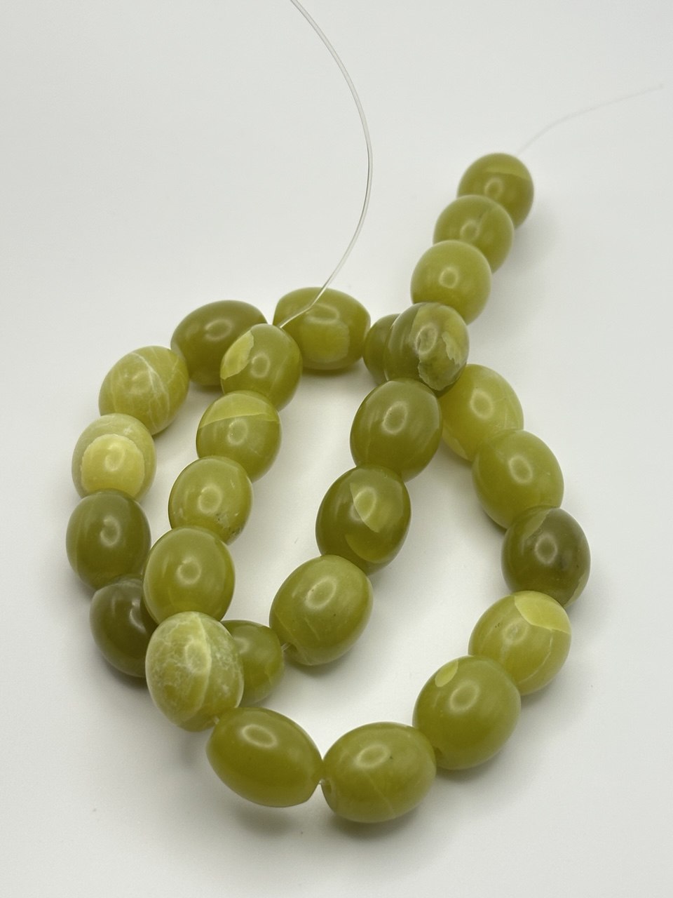 A string of olive green oval puffed serpentine beads on a white surface