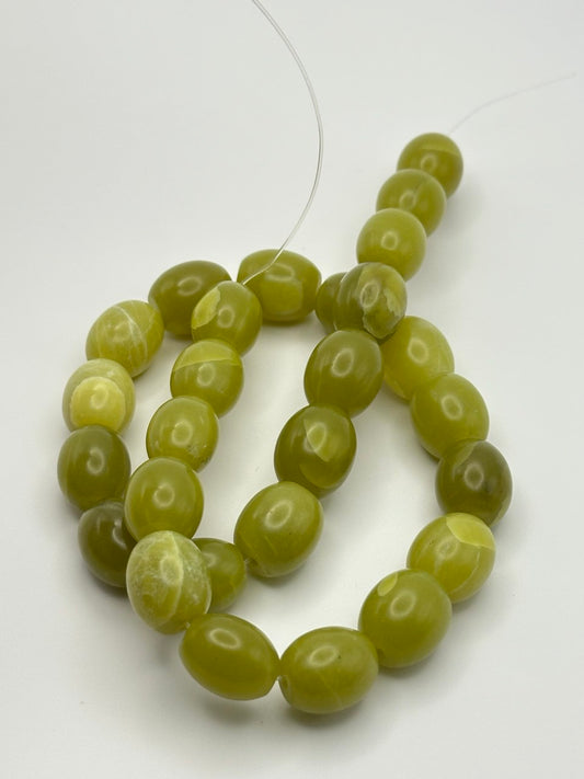 A string of olive green oval puffed serpentine beads on a white surface