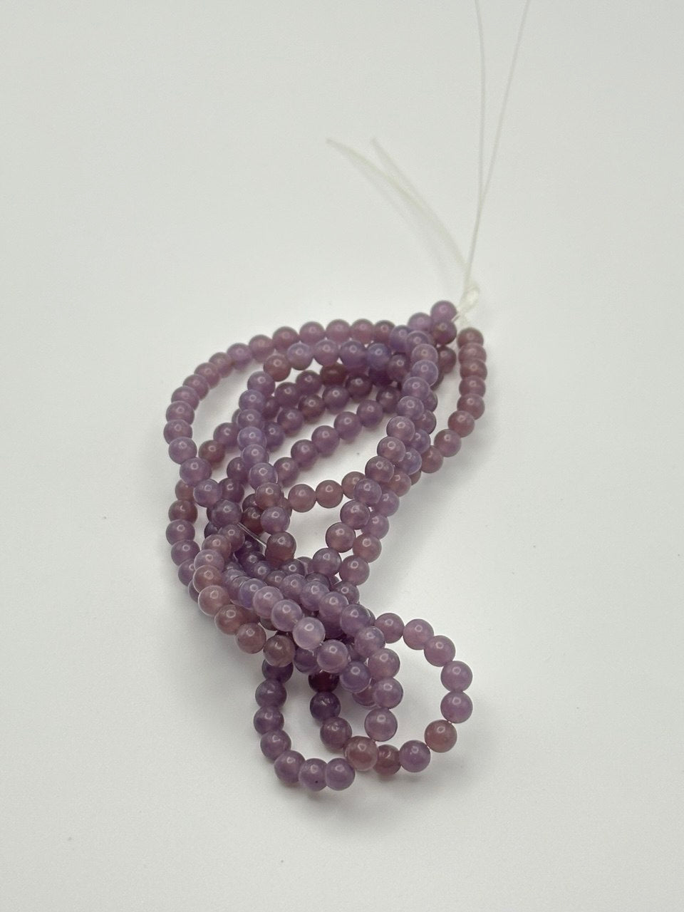 A string of lavender semi-transparent round smooth lepidolite beads on a white surface